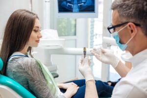 Dentist showing a dental implant to a woman with long brown hair