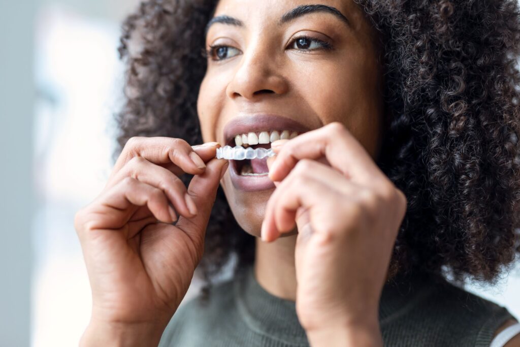 Woman in gray sweater vest inserting Invisalign over upper arch